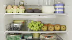 Three fridge shelves full of food like eggs, milk and strawberries